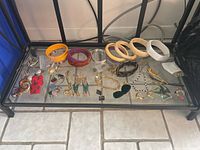 Full view of the jewelry lot displayed on a glass surface, showing bracelets, earrings, brooches.