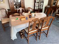 Wide angled image showing five wooden dining chairs around a wood dining table with items on the table, upholstery and carved wood details visible.