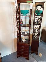 Full front view of wood display cabinet with decorative wooden supports and three open shelves containing various small decorative items.