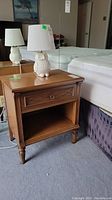 Front view of wooden bedside table with single drawer, open cubby and lamp on top