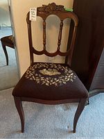 Front view of the wooden chair showing the carved backrest and needlepoint floral seat upholstery