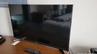 Samsung 32-inch flat screen TV on wooden table with remote nearby, screen off.