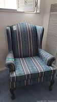 Full view of vintage wingback chair showing blue striped upholstery and wood legs.