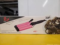 Photo of boxed Junima hair waver triple barrel styling tool, pink and black design with model's wavy hair shown on packaging.