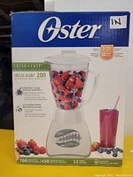 Front side of the original box showing Oster Precise Blend 200 blender with berries in glass jar, specifying 700 watts motor and 12 speeds.