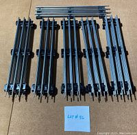Top-down view of 11 straight Lionel O gauge train tracks laid out parallel on a cardboard surface with a note 'Lot # 86'. Tracks are silver metal rails with black plastic ties, clean with no rust.