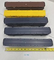 Top view of five Lionel car carrier train cars in brown, yellow, and dark blue colors with measuring tape indicating length.