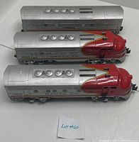 Top-down view of three Lionel Santa Fe F3 model train cars showing roof vent details. Two locomotives with red noses and one silver passenger car.