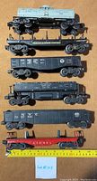 Six Lionel train cars displayed upright showing sides and markings including tank car, flatcar, gondola cars and red flatcar base.