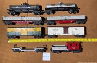 Top-down view of the eight Lionel O Gauge train cars laid out, showing all vehicles in detail from above.