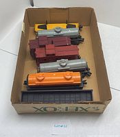 Photo of eight Lionel train cars inside cardboard box showing tops including several tank cars and flatcars.