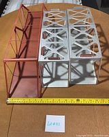 Three metal model train bridges on a table, two white with logos and one red bridge, with measuring tape showing size.