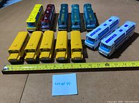 Top-down view of 15 pullback toy buses in various colors arranged in rows with measuring tape for scale.