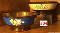 Pair of copper lustre ware bowls side by side, one yellow band and one blue band, both with raised floral decorations.