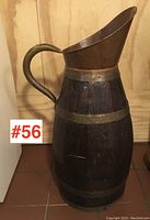 Front angle view of the large hardwood and metal antique jug showing the copper spout and brass handle