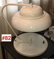 Photo showing the lamp at a side angle highlighting the curved arm connecting the dome shade to the circular base.