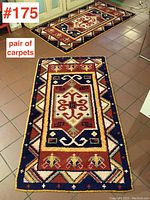 Pair of small carpets laid out on tile floor showing geometric and floral patterns in earth tones and dark borders