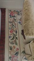 Floral area rug with cream background and flower border beside beige couch on tiled floor.