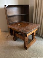 Three tier bookshelf with dark finish behind rustic pine table with rounded corners and solid wood top