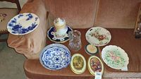 Lot shown on a sofa including blue and white china plates, floral plates, biscuit jar with lid, glass pitcher, two oval framed plaques, and small trinket box.