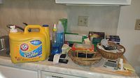 Overview of cleaning supplies, baskets, light bulbs, office supplies on kitchen counter