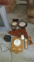 Overview photo of all items: four clocks, two clock radios, one clock mounted on live edge wood, two barometers; all with cords and various wooden casings.