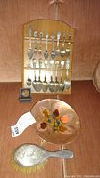 Wooden rack holding sixteen collectible spoons, one sterling handled brush, and California cloisonne plate laid in front