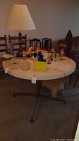 Photo showing round dining table with smooth white top surface and various household items on top (not included). Metal legs lightly colored in bronze/dark gold extending from a central post.
