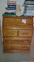 Front view of oak drop front desk showing closed drop front panel with three drawers below and books stacked on top.