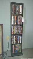 Full view of black wooden DVD storage shelf filled with DVDs from top to bottom.