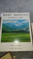 Framed John Ward Rocky Mountain National Park poster from 1992 calendar, showing landscape and signature.
