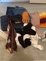 Photo of four pairs of men's jeans, assorted socks, gloves, ties, and a black Rockies cap arranged on floor.