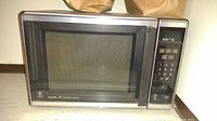 Front view of GE Dual Wave Microwave showing the large window and control panel with numeric keypad and function buttons.