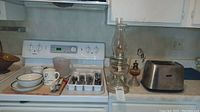 Oil lamps, toaster, flatware, and dishware on kitchen stove counter.