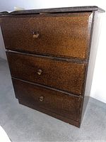 Front view of the small three drawer chest showing the textured brown finish and round drawer knobs
