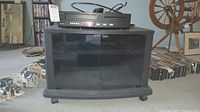 Philips VHS/DVD player sitting on top of a black TV stand with double glass doors and visible power cable and remote control on top.