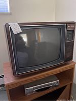Full view of vintage Zenith tube color TV sitting on wooden stand with silver Sanyo VCR player below
