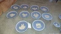 All ten Wedgwood Christmas collectible plates arranged on carpet, each plate showing detailed blue jasperware with white relief festive designs and wall hangers attached.