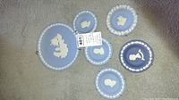 Six Wedgwood blue jasperware collectible plates arranged on carpeted floor: one large Apollo 11 plate, three presidential portraits, two other decorative classical relief plates. All plates have wall hangers attached.