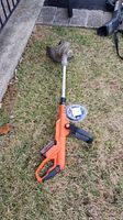 Full view of the Black & Decker orange string trimmer laying on grass showing the main body, shaft, and trimmer head with guard.