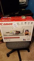 Front view of the Canon Pixma TS3122 printer box on a chair, showing brand and model.