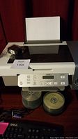 Lexmark printer with paper loaded, black Lexmark ink cartridge sealed on top, two spindle packs of blank CDs, Dell keyboard, cables on desk