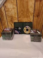 Photo showing two stacks of PlayStation 2 game cases with discs, plus one open case showing a game disc inside.