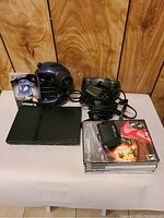 Full lot with PlayStation 2 console, controllers, games, memory cards, and power cord on white surface against wood panel background.