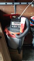 Front and side view of Ridgid wet/dry vacuum showing hose and label details.