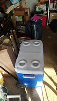 Photo showing the cooler closed, highlighting the split lid with four cup holders, wheels, and the handle.