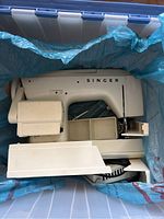 Singer 2430 sewing machine in storage bin, showing overall condition and accessories storage.