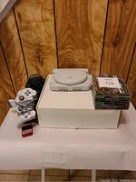 Sony PS One console closed, two white controllers coiled, black cable behind, red memory card in front, stack of game cases