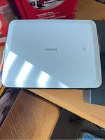 White Philips DVD player with top-loading lid on a wooden surface.
