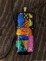 Close-up front view of rectangular black art glass pendant with colorful reflective geometric patterns on dark wood background.